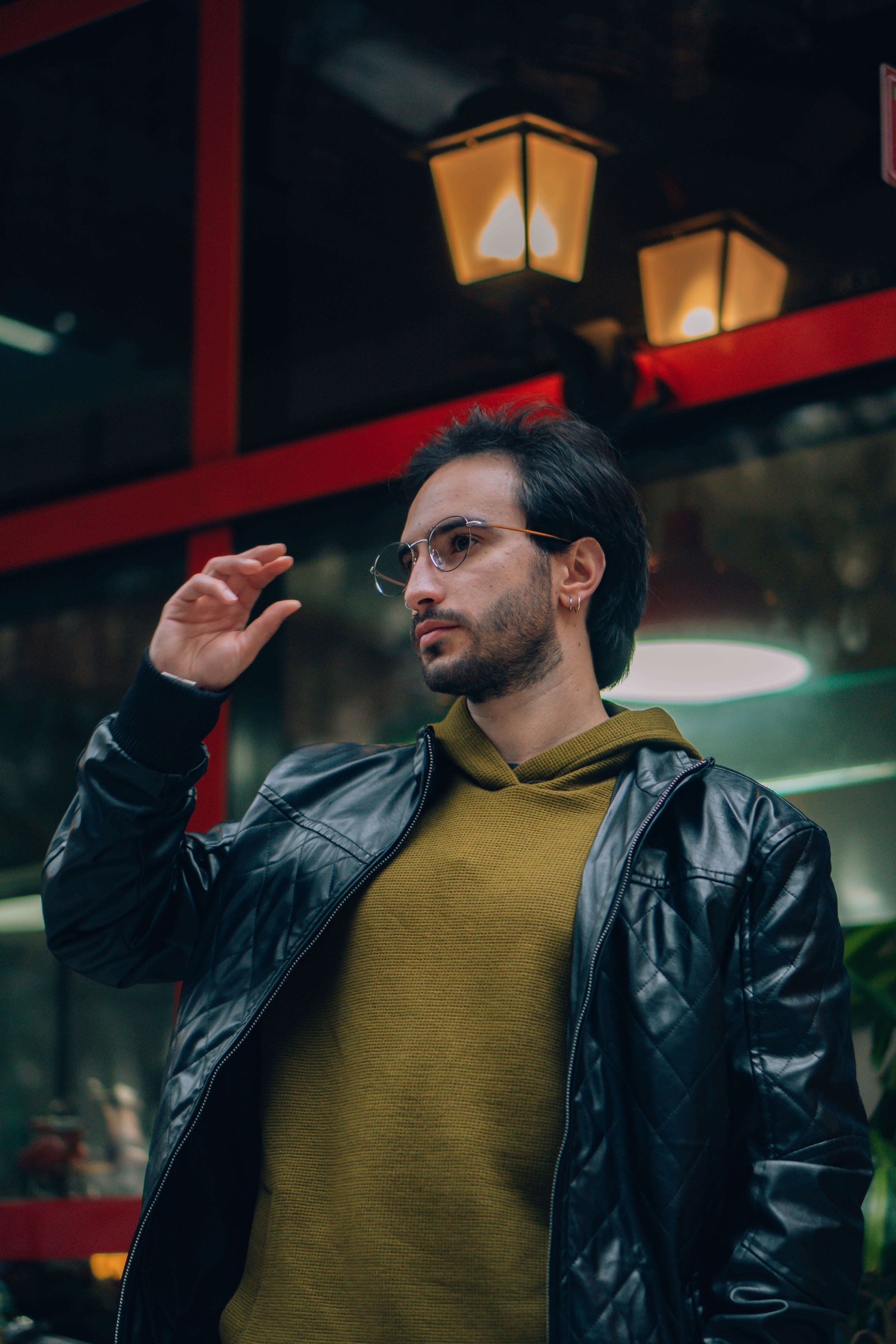 Homem com óculos de grau e jaqueta de couro caminhando na rua, olhando para o lado.