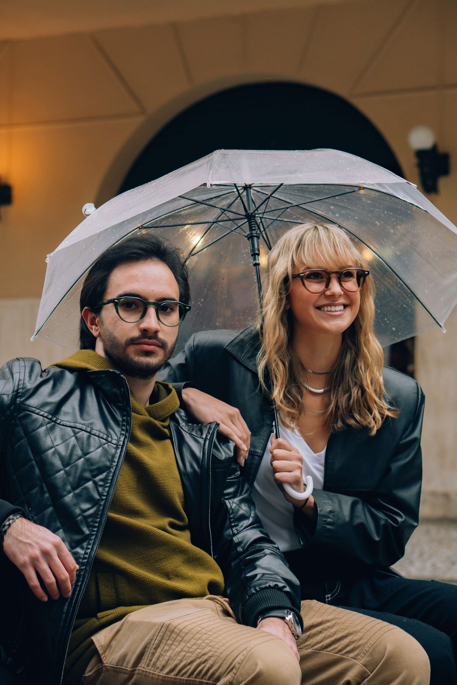 Duas pessoas se protegendo da chuva com um guarda-chuva, com muito estilo e a qualidade que a Ótica OART oferece.