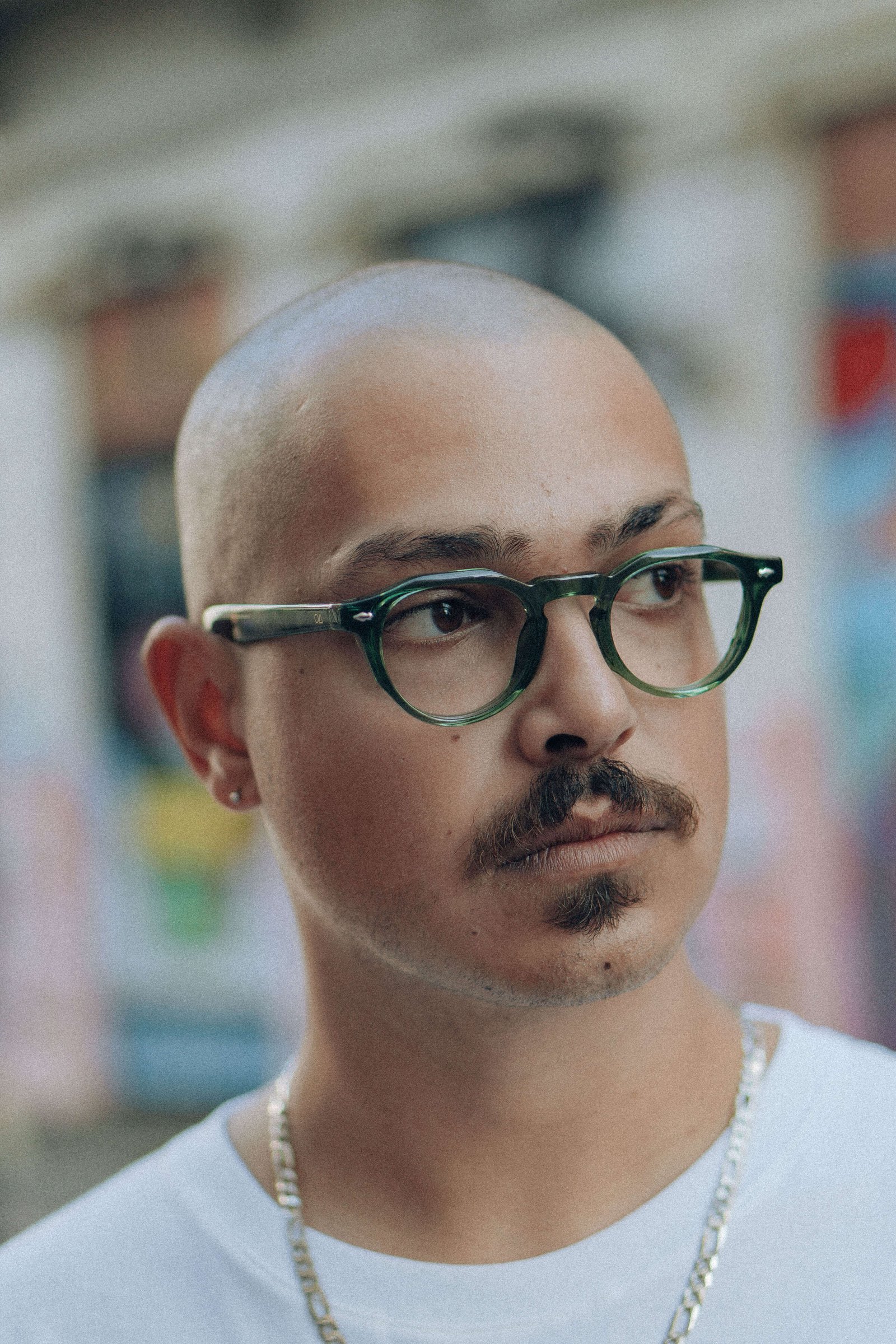 Retrato fechado de homem careca com bigode e óculos de grau olhando para o lado em ambiente interno.