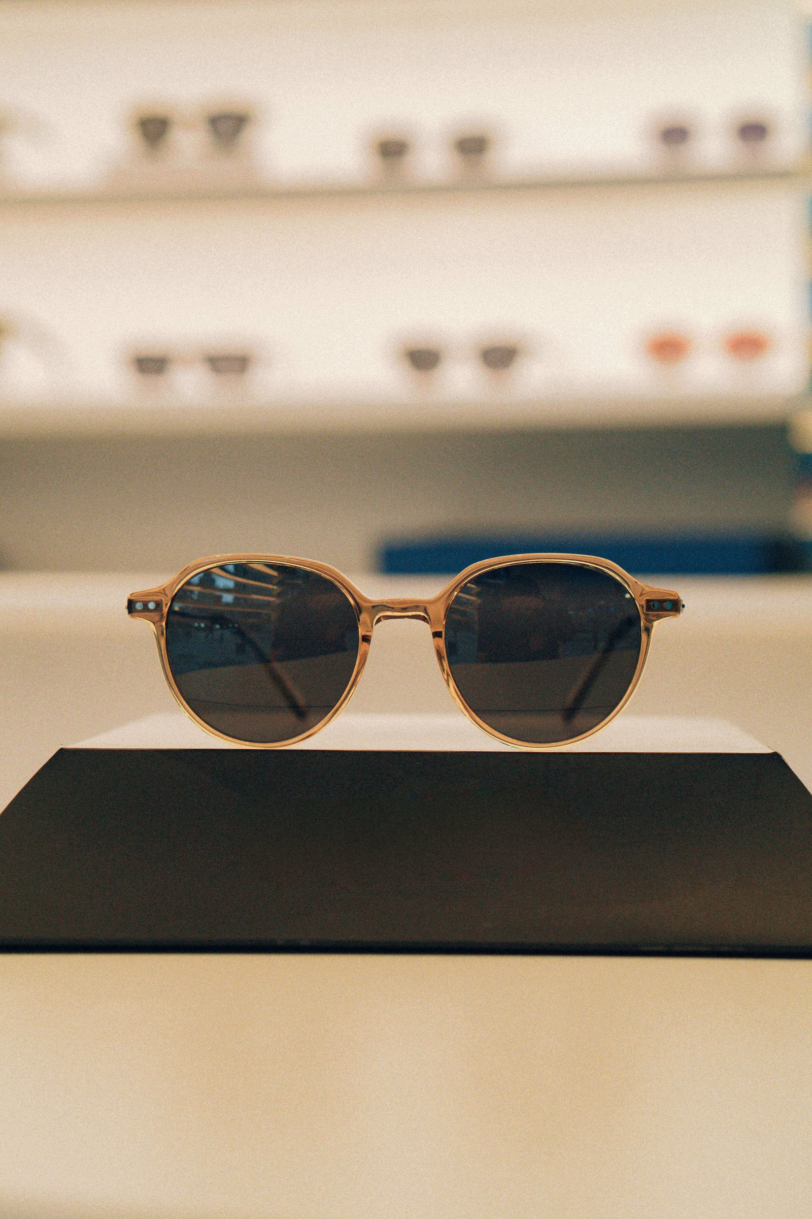 Óculos de sol com armação dourada e lentes escuras apoiados em suporte preto na loja.