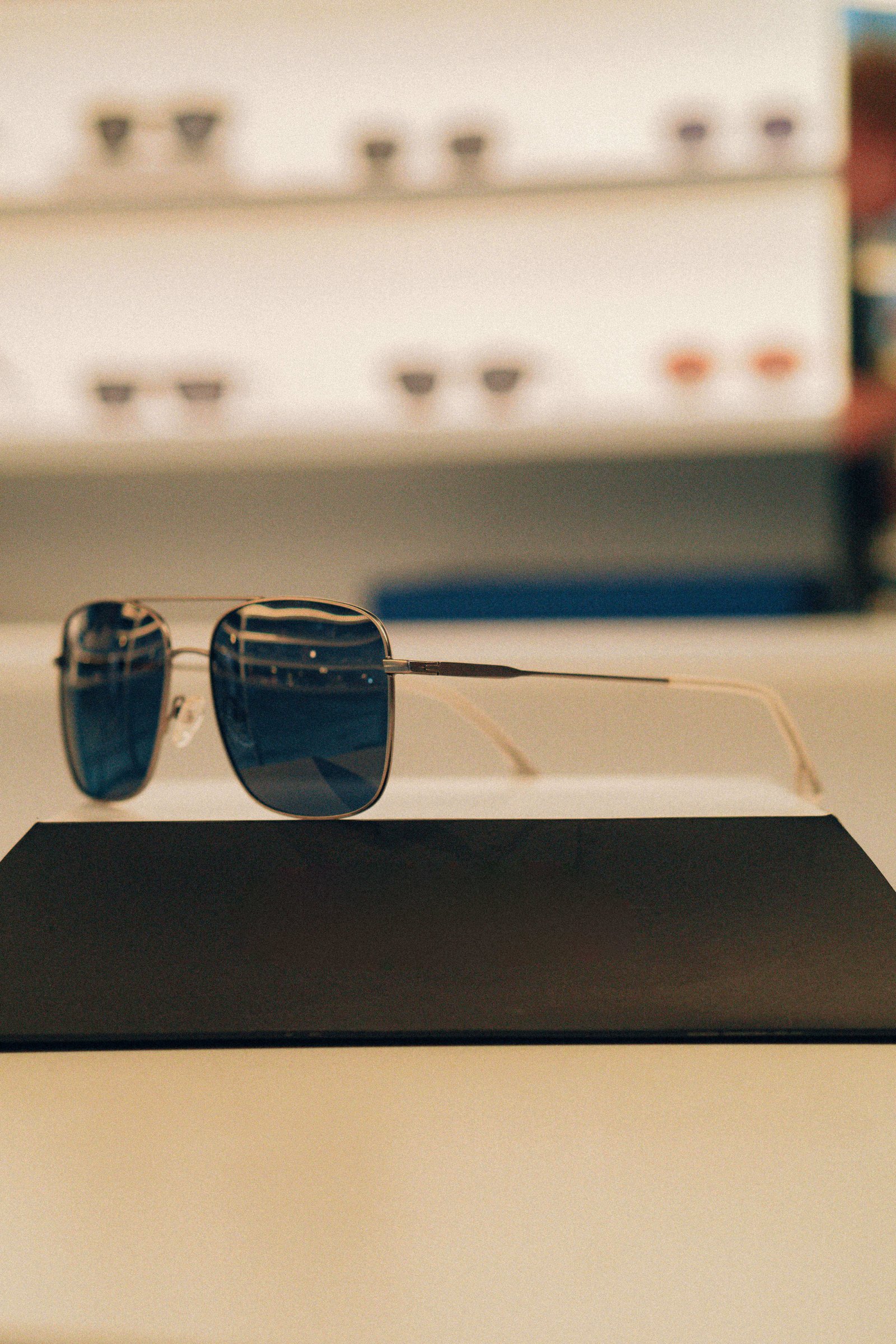 Dois óculos de sol, um gatinho e outro arredondado, posicionados lado a lado sobre suporte na ótica.