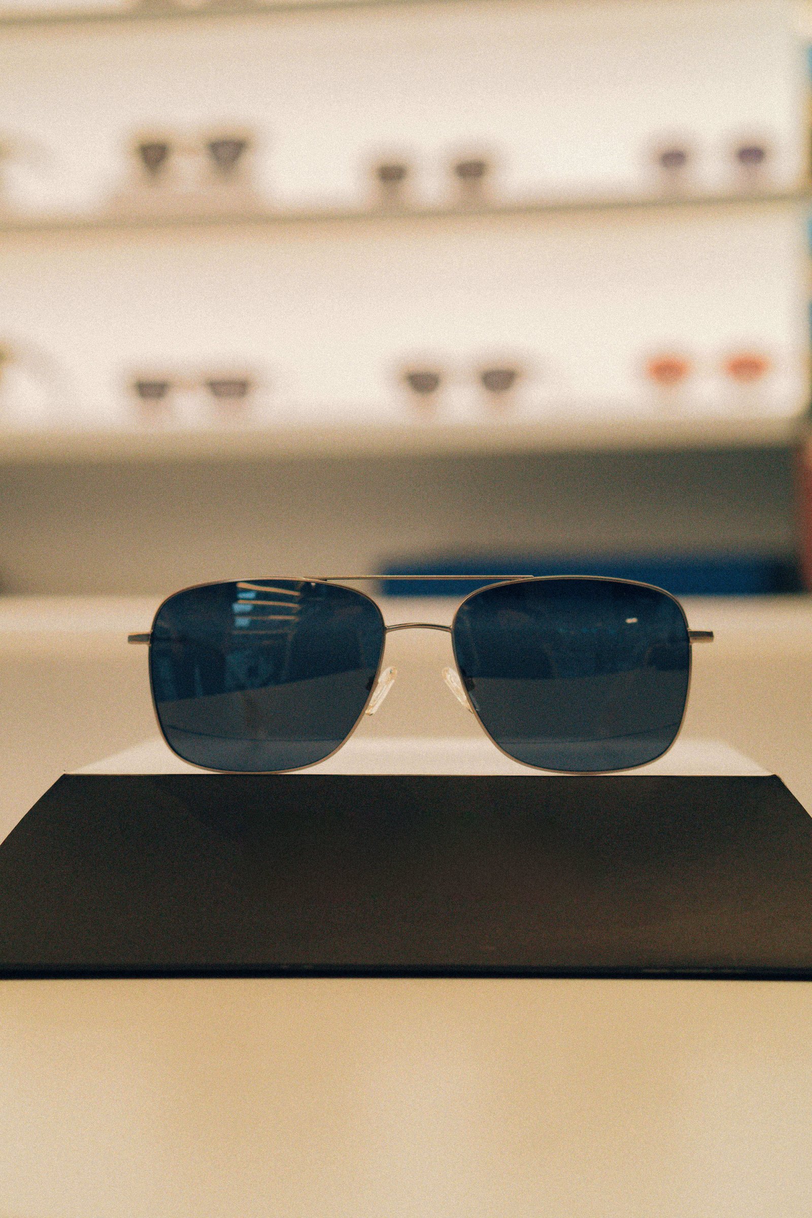 Óculos de sol de lentes arredondadas escuras sobre base preta em vitrine minimalista.