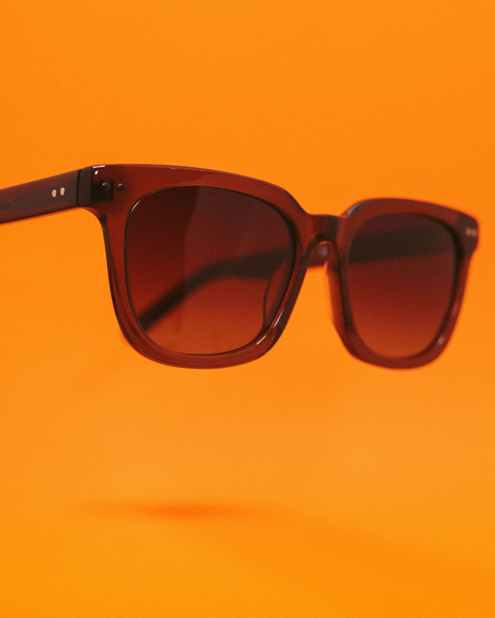 Óculos de sol quadrado marrom fotografado em fundo laranja.