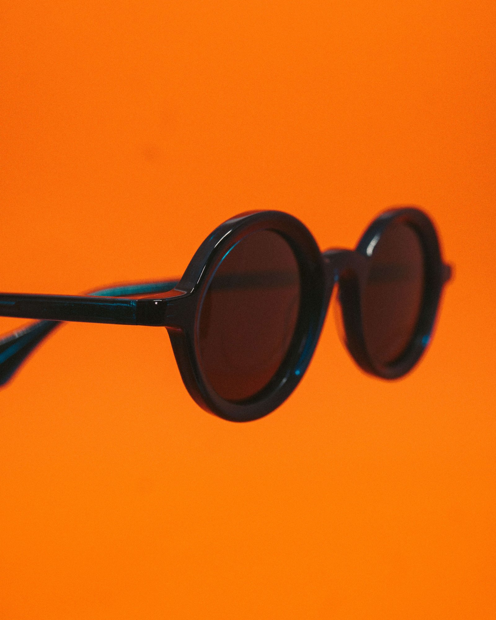 Óculos de sol redondo escuro em destaque sobre fundo laranja.